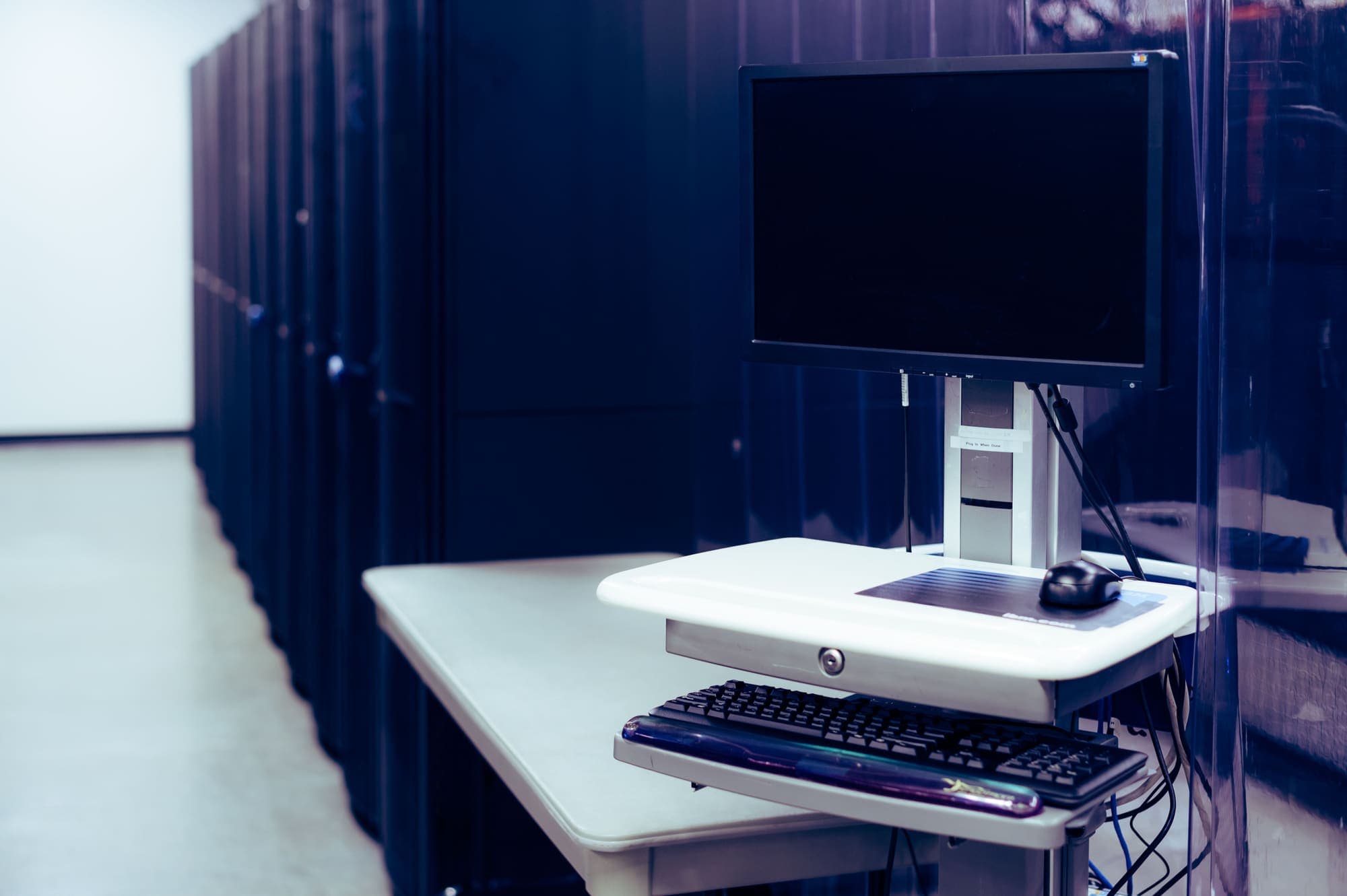 A workstation cart with a monitor and keyboard in a data center aisle.
