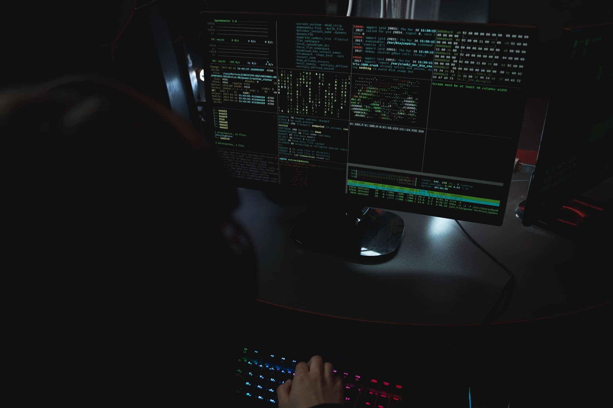 A person at a keyboard in a dark room, facing a monitor of terminal windows.